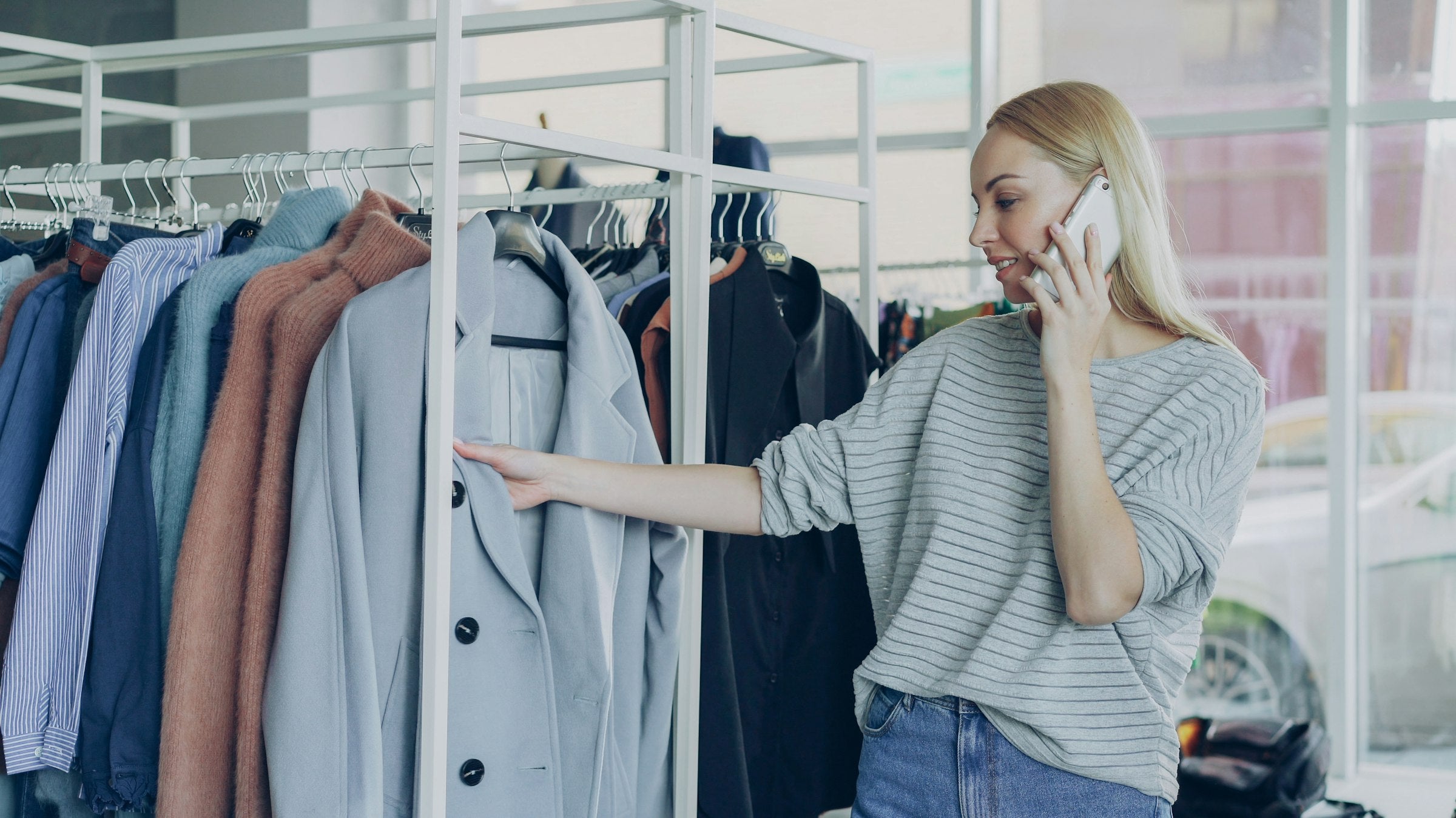 A shopper browsing a rail of clothing in a boutique while using her phone, illustrating the link between store discovery and digital retention